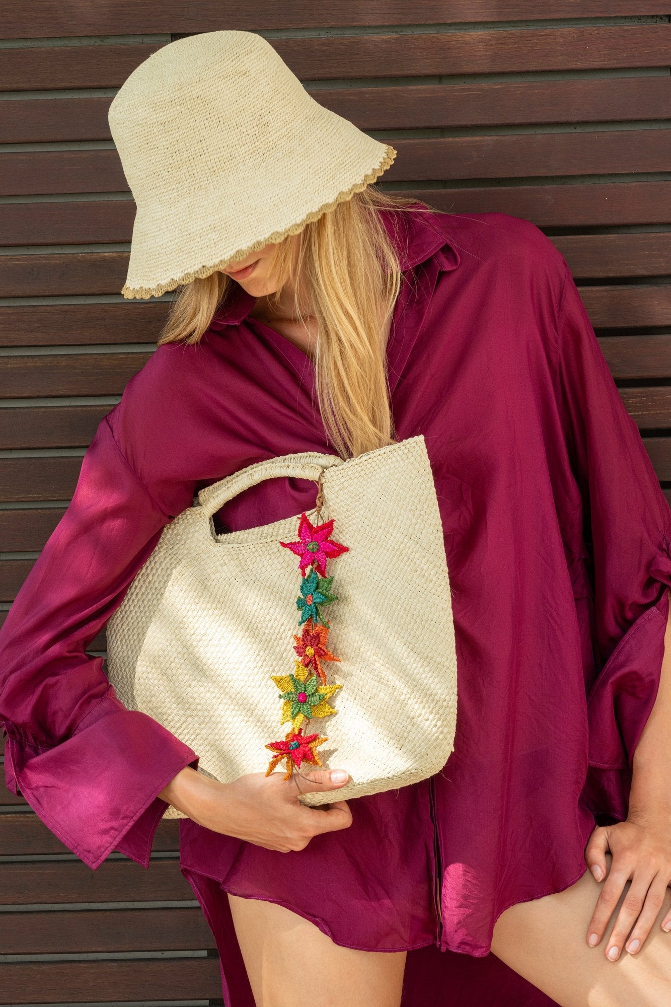 The Sierra bucket hat in yellow, worn with a burgundy blouse and a flower-trimmed straw tote